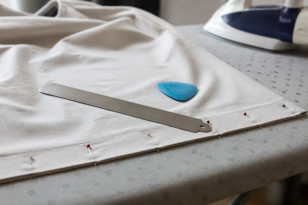 Bas de jupe en coton épinglé et repassé sur une planche, réglette d’ourlet graduée et craie tailleur posées à côté